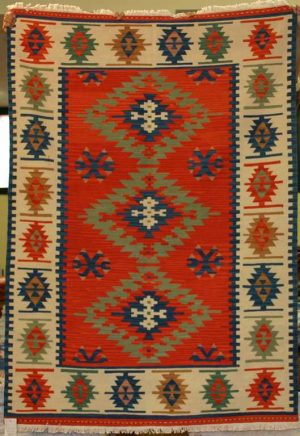 Tappeto contemporaneo kilim lana con triplo medaglione centrale uncinato su fondo rosso e motivi decorativi geometrici astratti su bordo bianco spesso