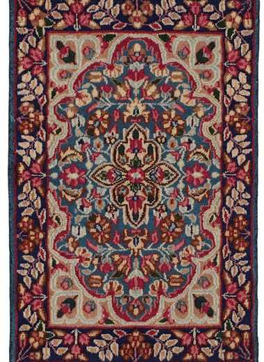 Tappeto persiano Kirman, con medaglione centrale decorato a motivi floreali, su sfondo blu e intricati dettagli decorativi sullo spesso bordo blu.