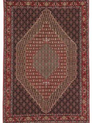 Tappeto persiano Sanandaj con medaglione centrale geometrico a rombo, su sfondo rosso, e motivi decorativi a rombi, herati e boteh a tutto campo