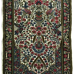tappeto persiano kirman con medaglione centrale a motivi floreali e animali, su sfondo bianco con piccoli fiori verdi, rosa e azzurri