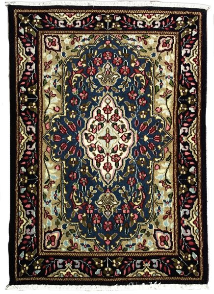 tappeto persiano kirman con medaglione centrale bianco a motivi floreali, su sfondo blu con piccoli fiori verdi, rosa e azzurri