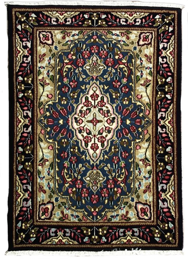 tappeto persiano kirman con medaglione centrale bianco a motivi floreali, su sfondo blu con piccoli fiori verdi, rosa e azzurri