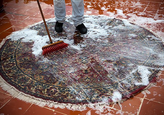 Man washing a rugs on the tile floor.