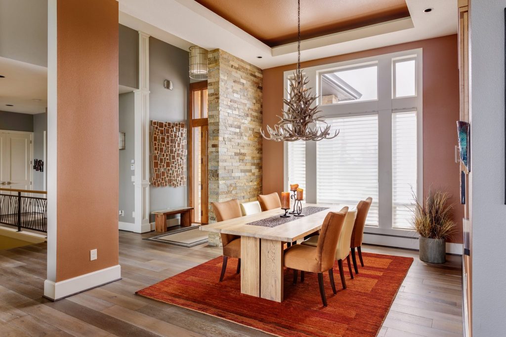Tappeto Artorient moderno rosso e arancio sotto tavola in sala da pranzo minimalista con elementi naturali come il parquet in legno e il muro in pietra