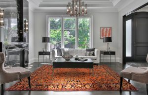 tappeto persiano antico color arancione in soggiorno neoclassico moderno bianco, sotto un tavolino nero e con due consolle ai lati